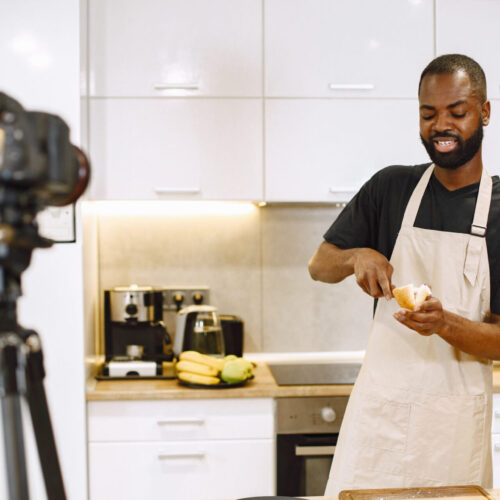 African-american bearded man smiling and cooking. Blogger shooting video for cooking vlog in kitchen at home.Man wearing an apron.